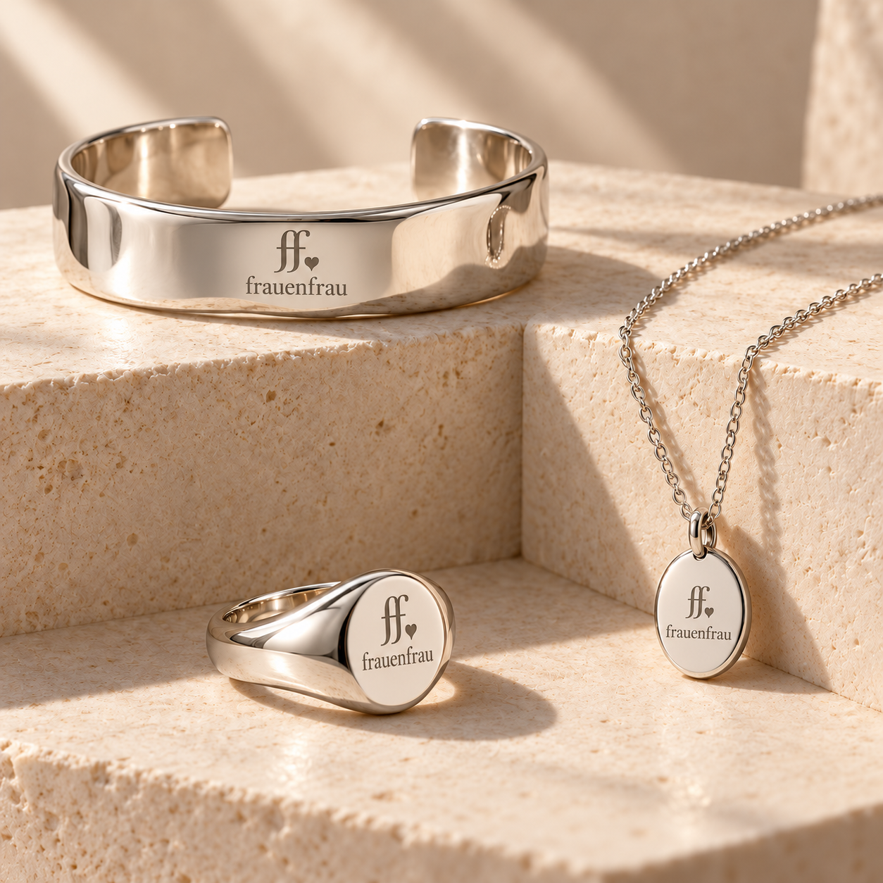 Drei silberne frauenfrau Schmuckentwürfe: Armreif, Ring und Halskette mit Anhänger, jeweils mit graviertem ff-Herz-Logo und frauenfrau Schriftzug